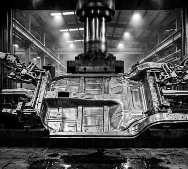 Large automotive chassis structural component being transferred between stamping stations by robotic transfer arms in a Tier 1 automotive supplier facility