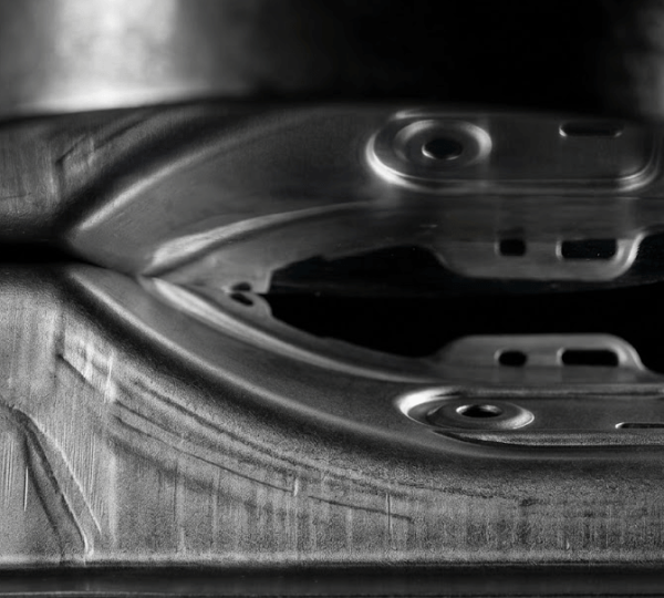 Deep-drawn B-pillar reinforcement component mid-stroke in transfer die stamping press showing compound curve geometry and robotic transfer arm grip points